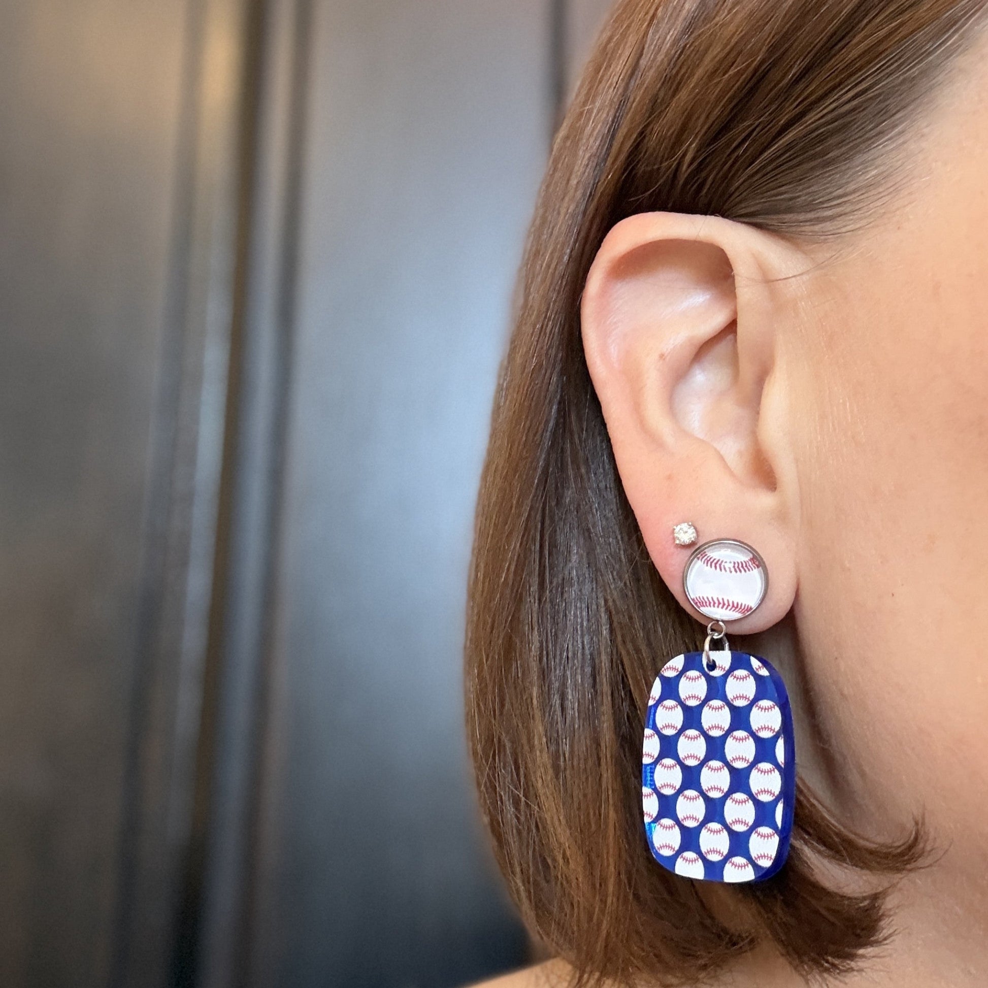 Model wearing Baseball mom earrings with blue mirror acrylic drops and repeating baseball pattern