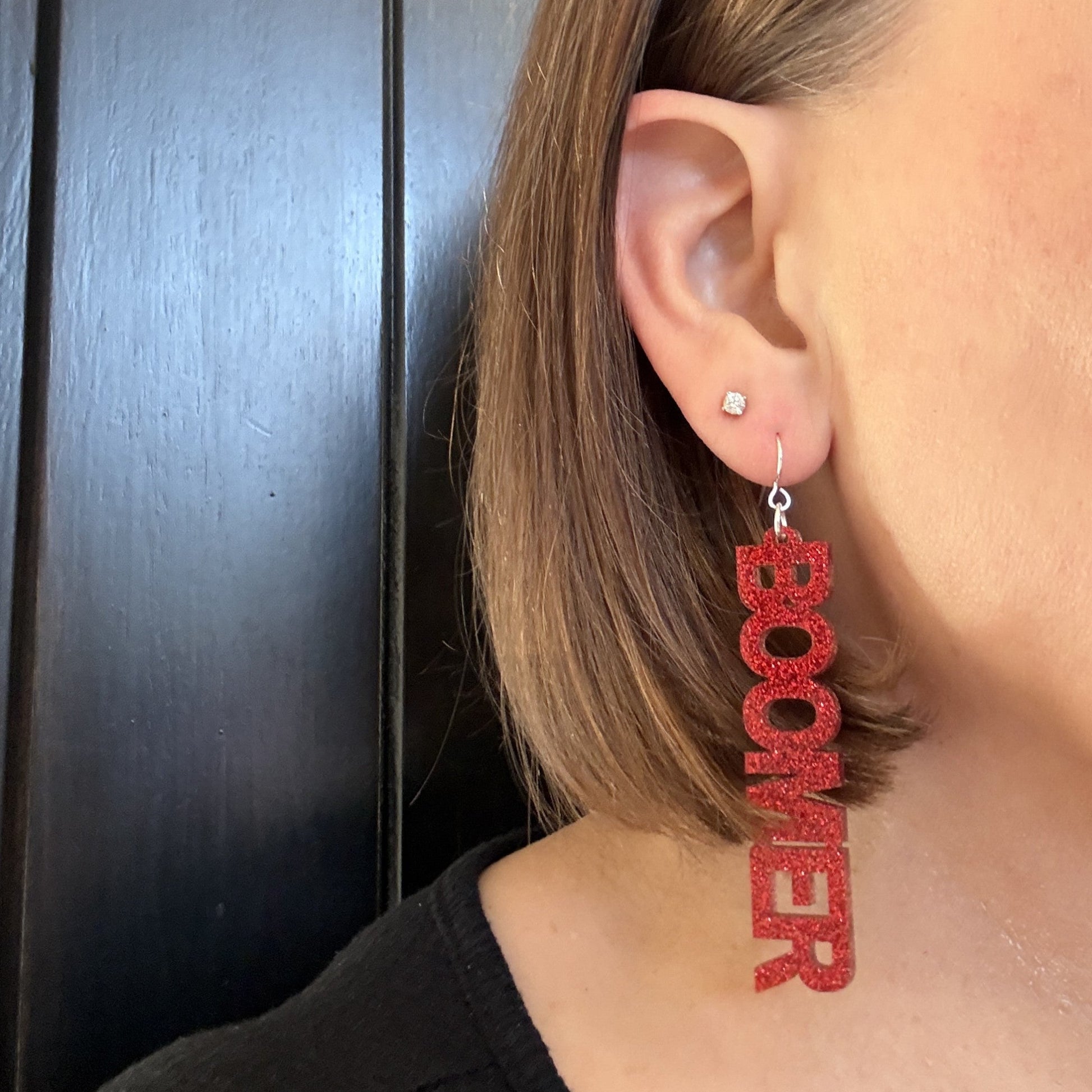 Model wearing Boomer Sooner dangle earrings in crimson glitter with silver-toned earring hooks