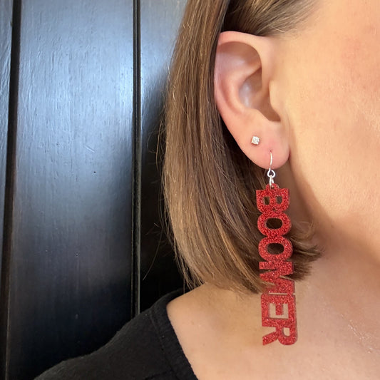 Model wearing Boomer Sooner dangle earrings in crimson glitter with silver-toned earring hooks