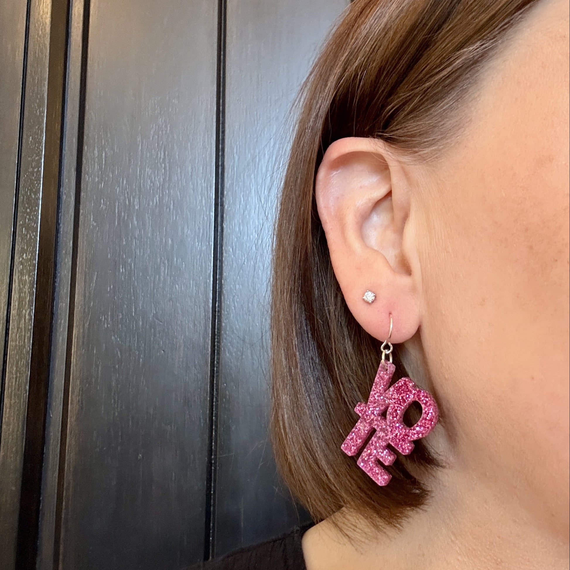 Model wearing vote earrings in bright pink glitter with silver-toned earring hooks
