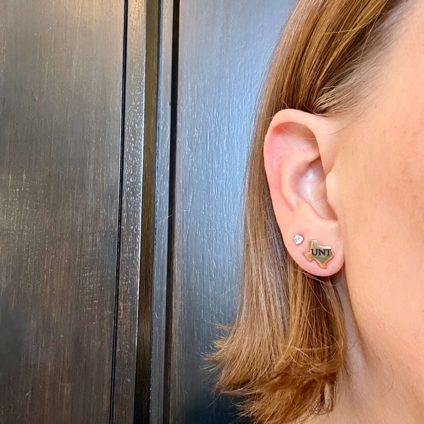 Model wearing gold-toned Texas-shaped UNT stud earrings