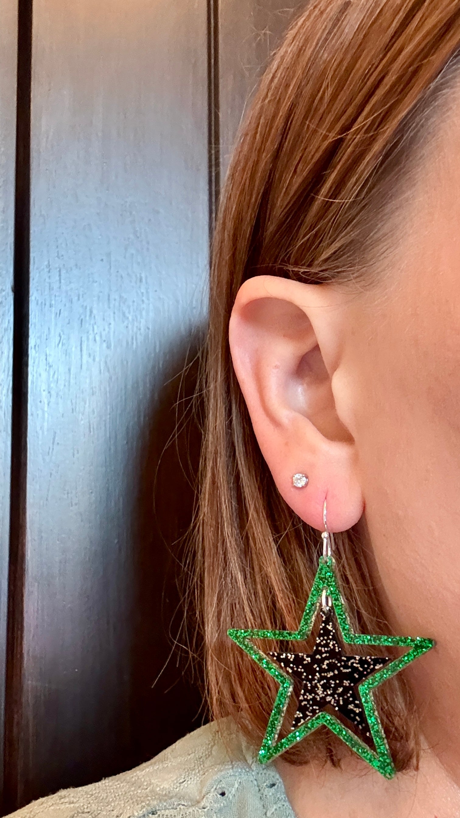 Model wearing Green and black glitter stars earrings on silver hooks, lightweight acrylic dangles for game day, handmade in Texas by half turn designs
