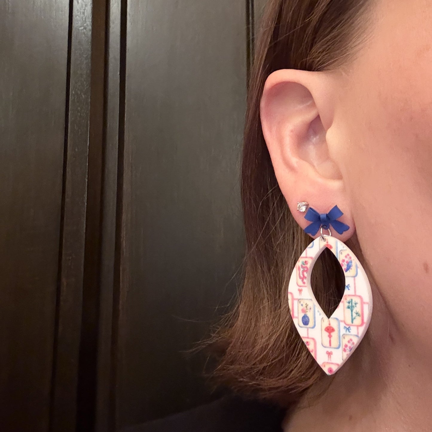Model wearing Mahjong tile earrings, white acrylic earrings with colorful mahjong print, topped with a blue bow