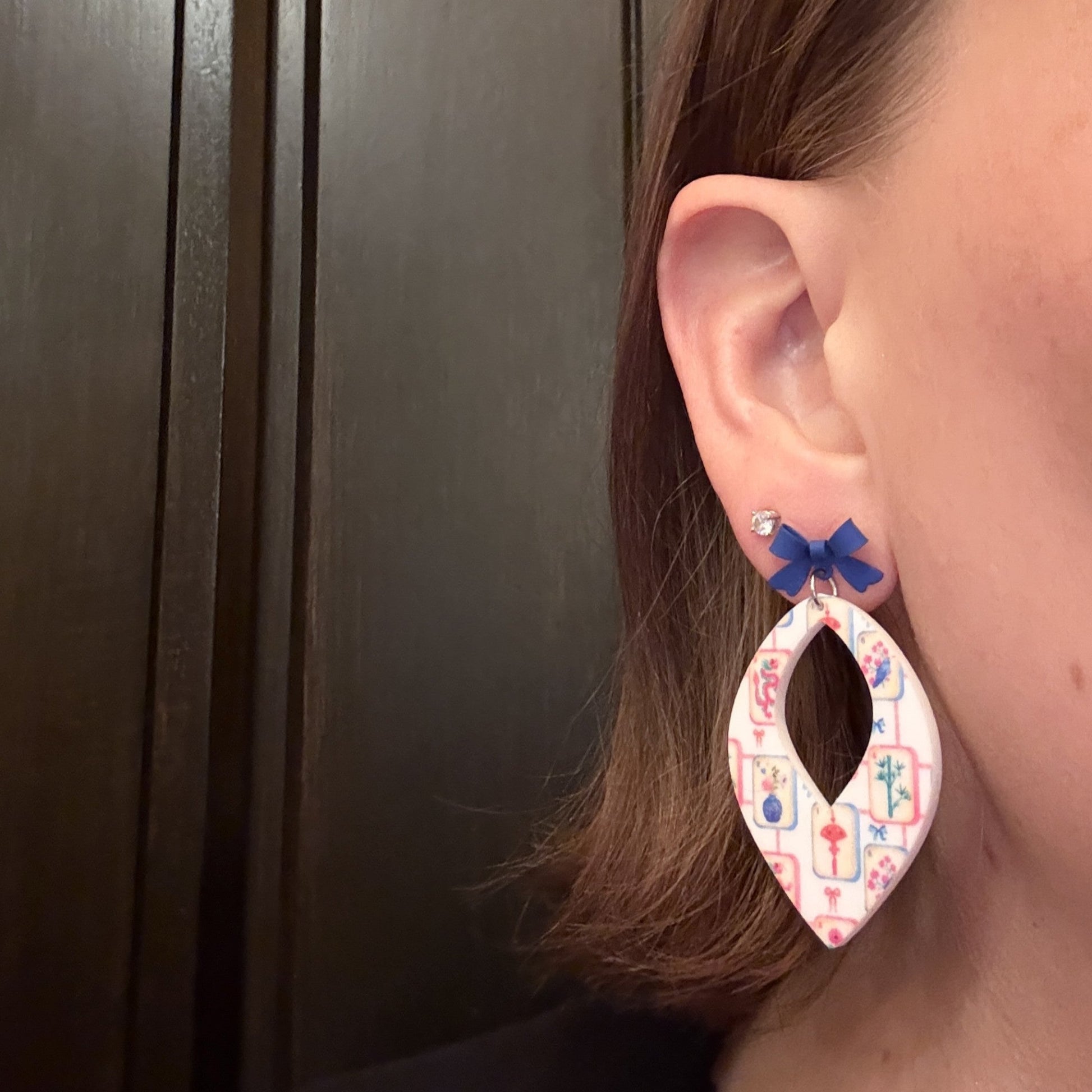 Model wearing Mahjong tile earrings, white acrylic earrings with colorful mahjong print, topped with a blue bow