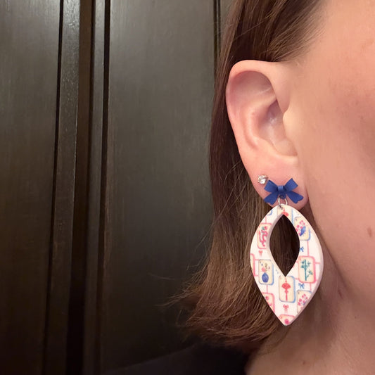 Model wearing Mahjong tile earrings, white acrylic earrings with colorful mahjong print, topped with a blue bow