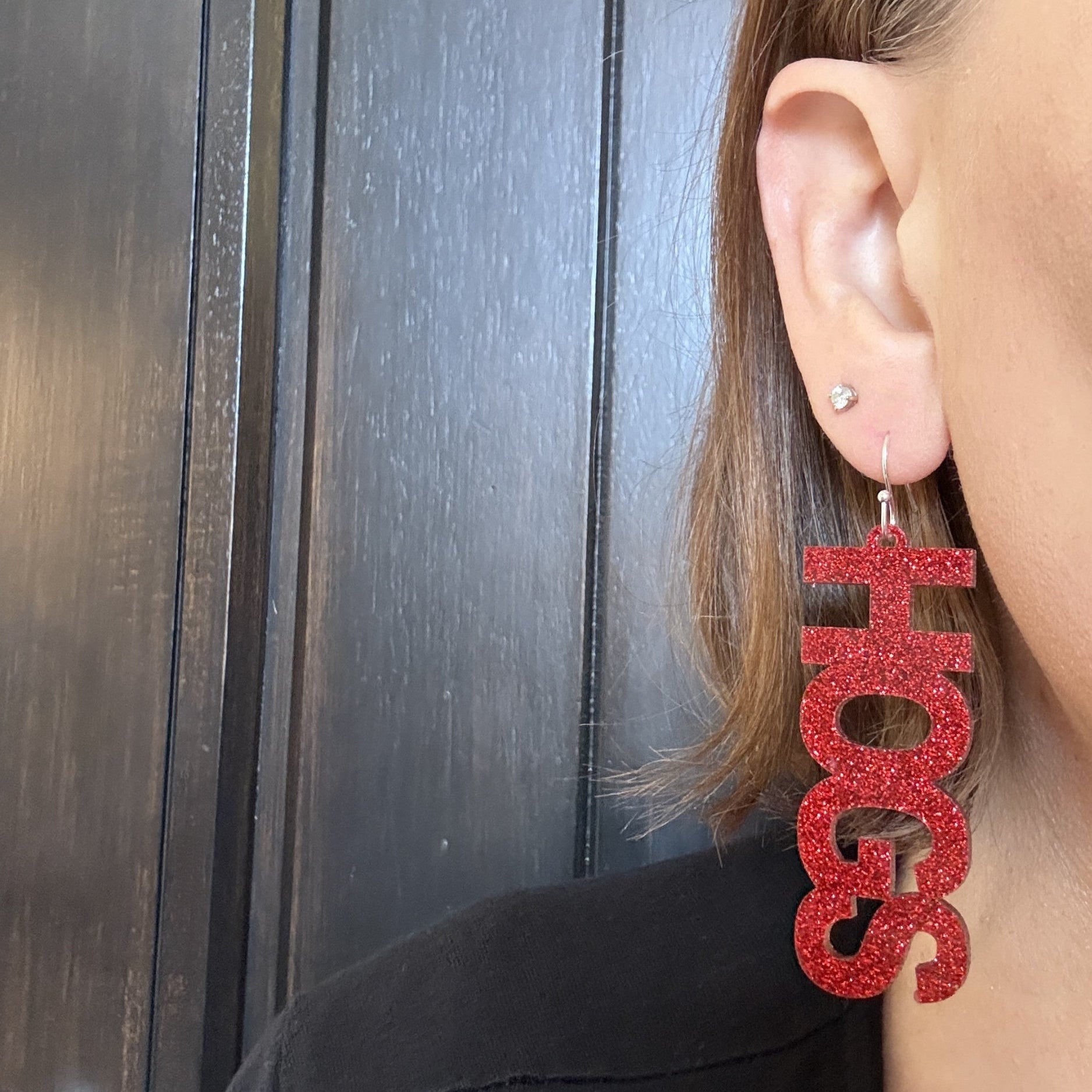 Model wearing University of Arkansas Game Day HOGS dangle earrings in crimson glitter acrylic with silver stainless steel earring hooks