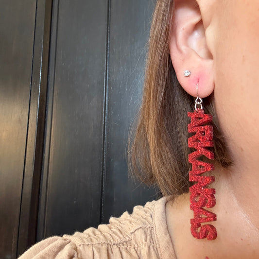 Model wearing Arkansas Razorbacks glitter word dangle earrings on silver hooks