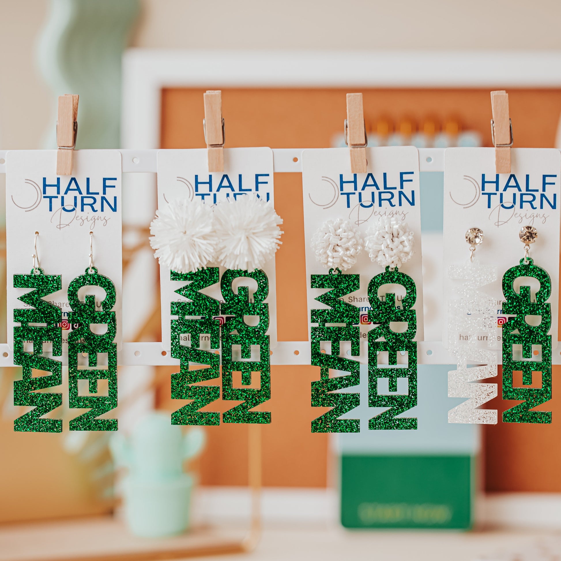 Large University of North Texas Mean Green glitter earrings, one spelling “MEAN” and the other “GREEN,” in green and white glitter with multiple topper options.