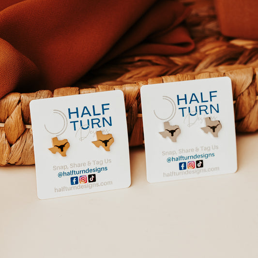 University of Texas stainless steel stud earrings shaped like the state of Texas, engraved with the Longhorn logo. Shown in 12mm size on Half Turn Designs branded earring cards, available in gold and silver finishes.