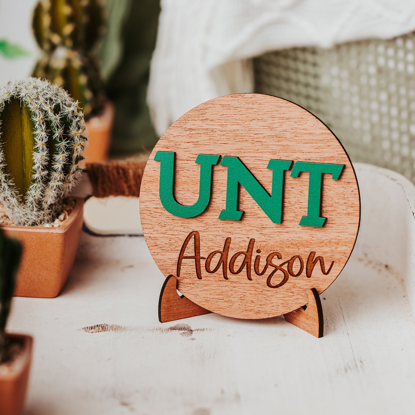 Officially licensed University of North Texas 5 inch round wooden dorm decor, shelf sitter and desk sign in mahogany wood with the UNT letters in Mean Green, personalized with your choice of 1-2 lines of engraved text in four wood finishes. Comes with a matching stand.