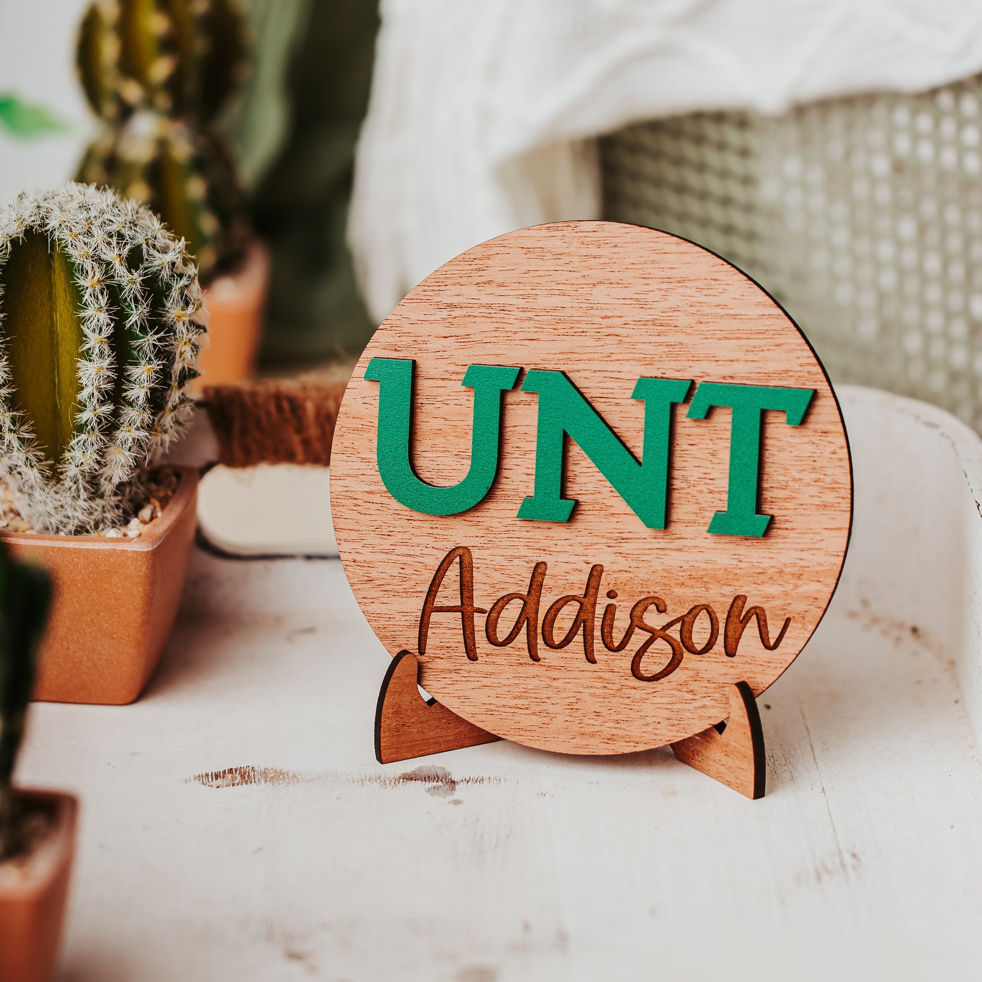 Officially licensed University of North Texas 5 inch round wooden dorm decor, shelf sitter and desk sign in mahogany wood with the UNT letters in Mean Green, personalized with your choice of 1-2 lines of engraved text in four wood finishes. Comes with a matching stand.