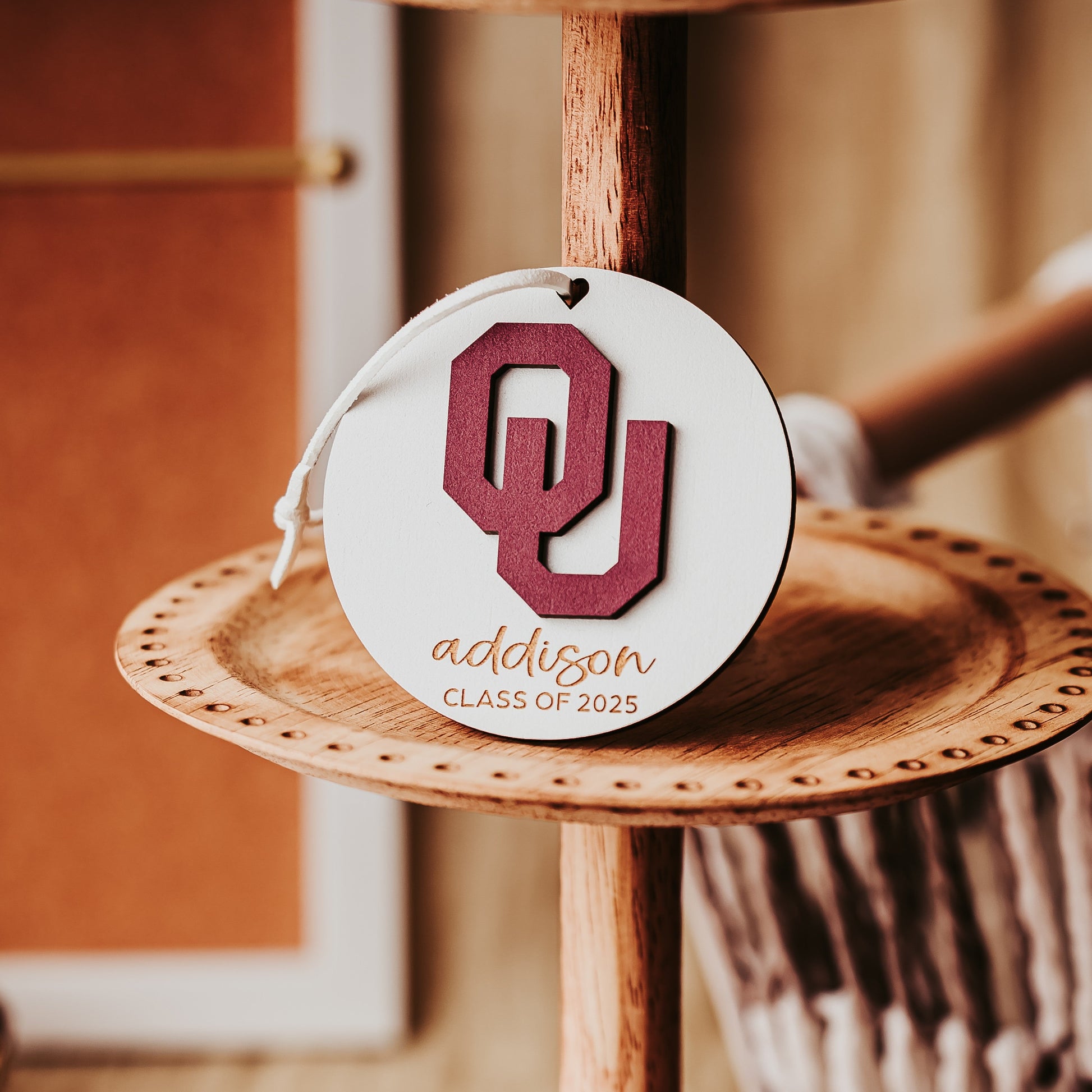 Engraved University of Oklahoma ornament featuring crimson OU logo on 3-inch round wood ornament, customizable with name or phrase, available in Cherry, Mahogany, Walnut, Sapele, or White finishes. Perfect Sooner Christmas gift or car charm. Shown here in White wood option.