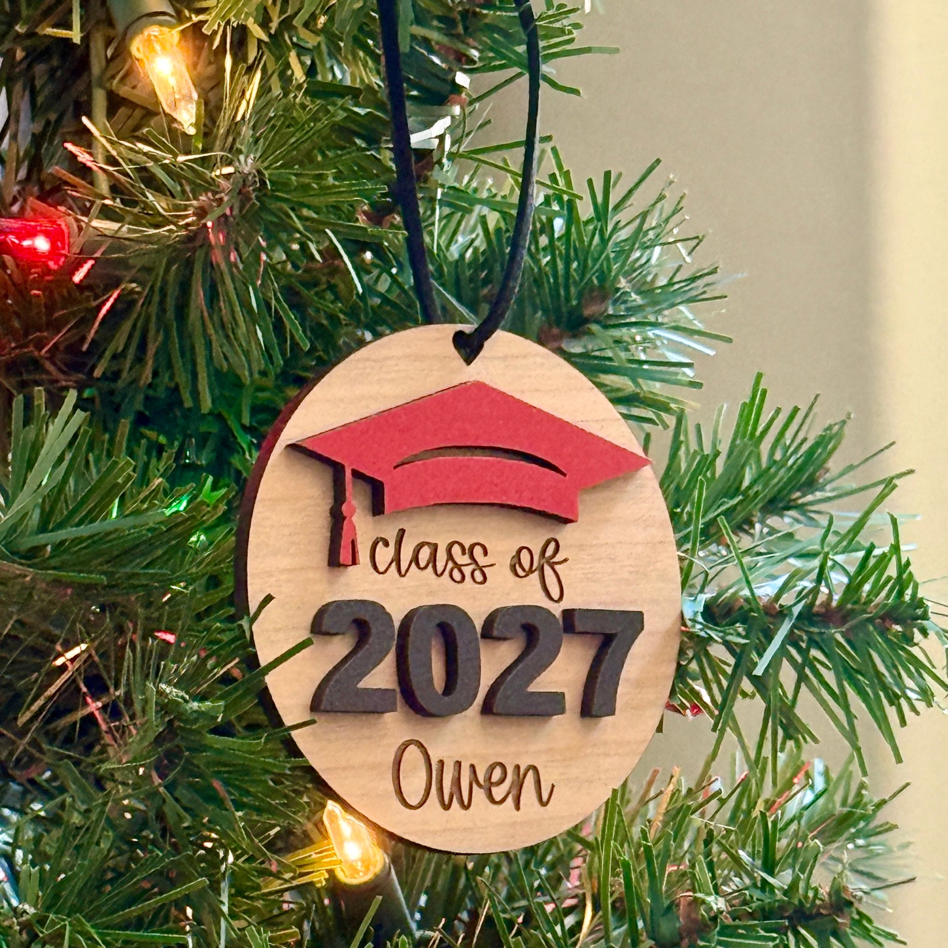 Class of 2027 wooden ornament in mahogany finish with red graduation cap, raised black 2027 numbers and graduate's engraved name