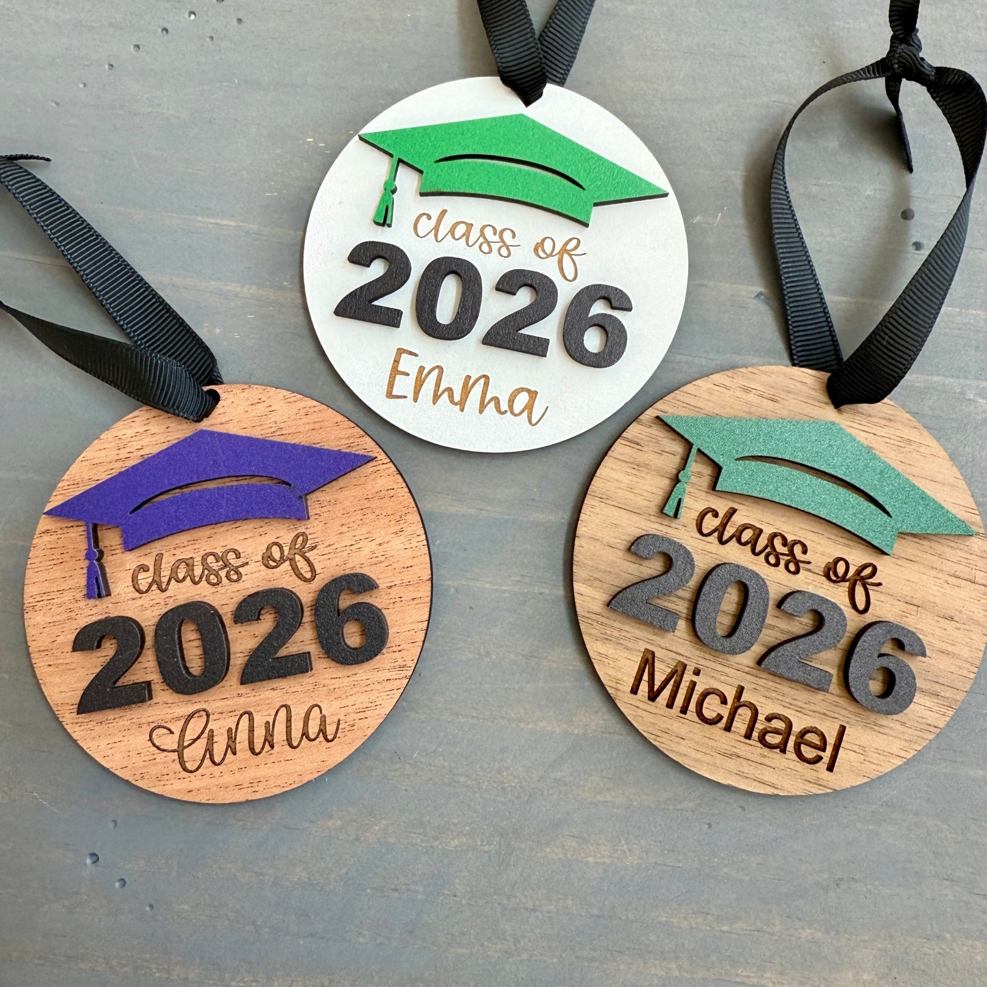 Personalized Class of 2026 ornament in white wood, engraved with the high school senior graduates name in three of the available styles from Half Turn Designs. 14 high school colors are available to further personalize the ornament with your choice of graduation cap color.