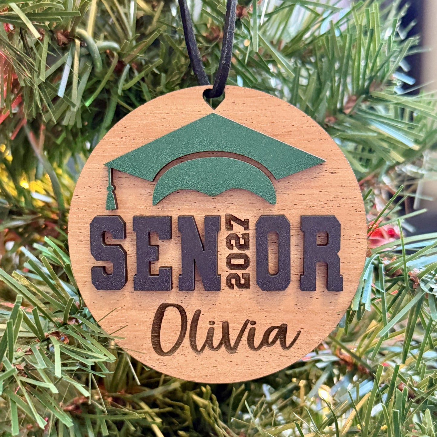 Personalized Senior 2027 wooden ornament in mahogany wood finish with green graduation cap, engraved with the graduate's name