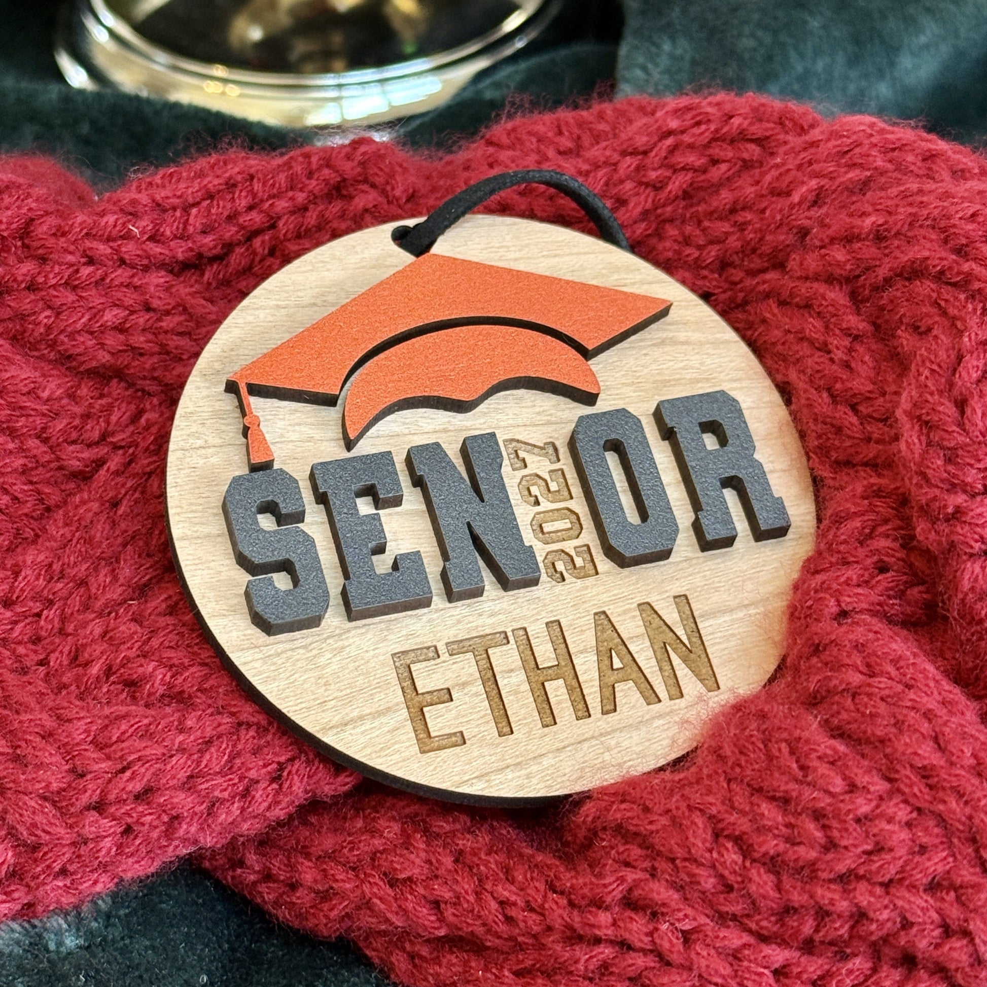 Personalized Senior 2027 wooden ornament in cherry finish with orange graduation cap, engraved with the graduate's name