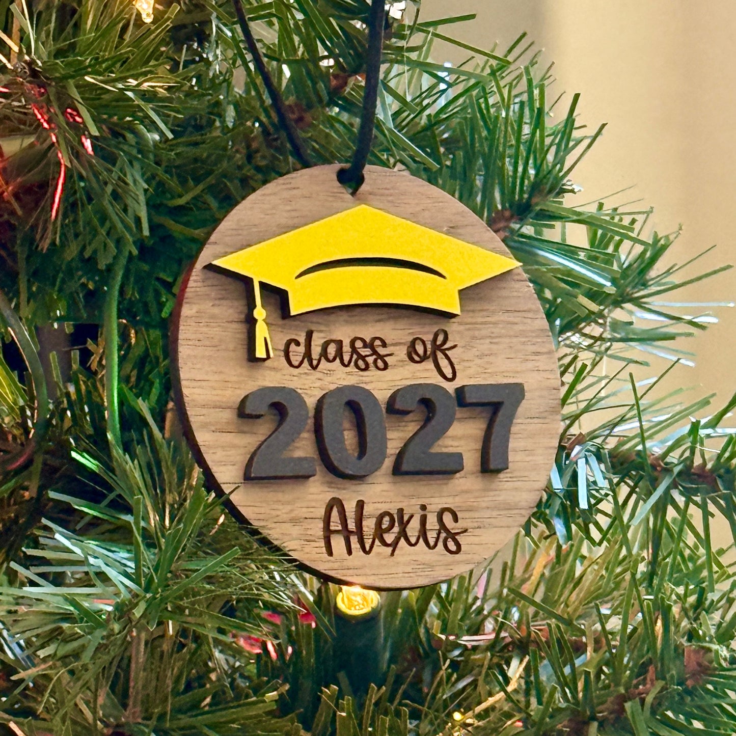 Personalized Class of 2027 wooden ornament in walnut finish with yellow graduation cap, raised black 2027 numbers and graduate's engraved name