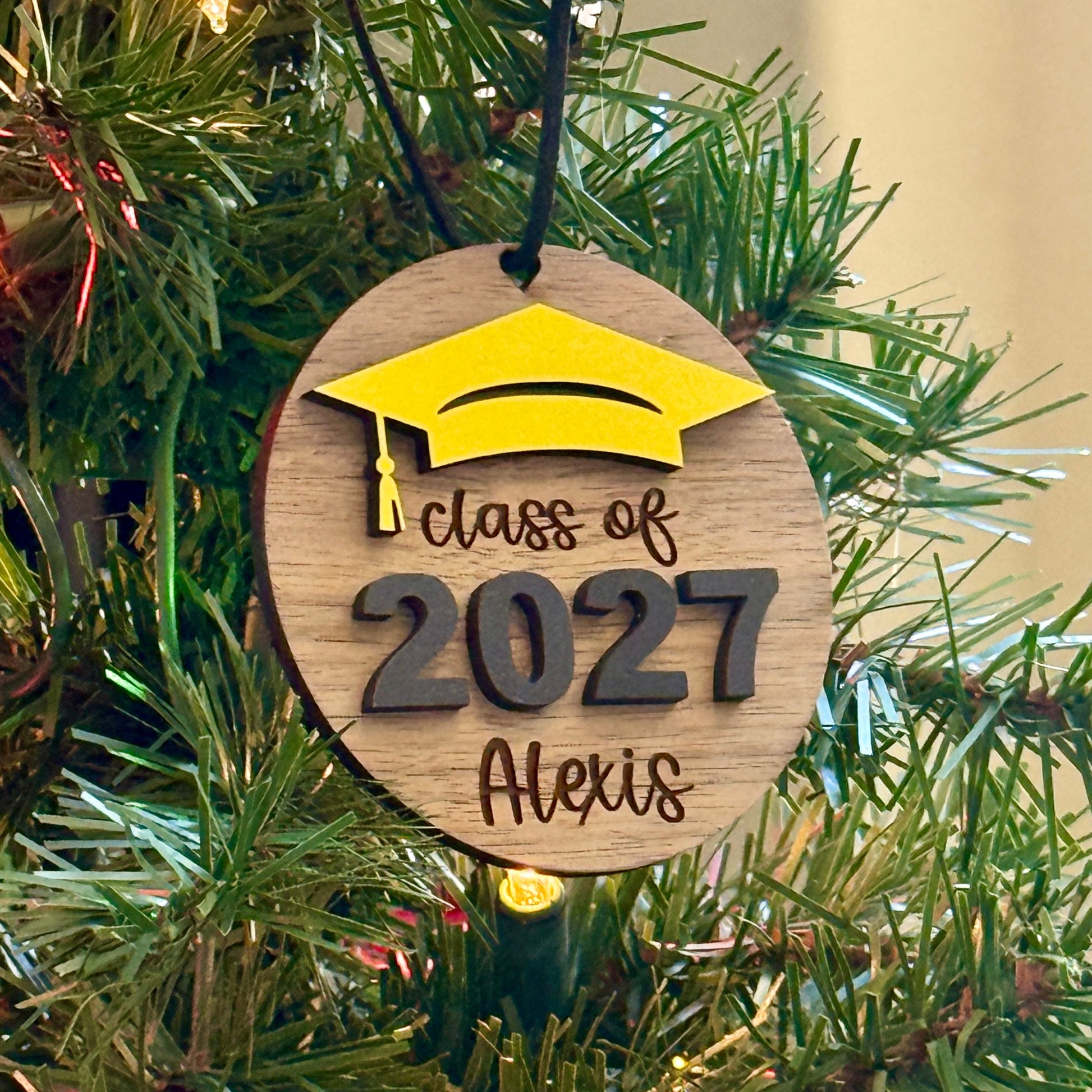 Personalized Class of 2027 wooden ornament in walnut finish with yellow graduation cap, raised black 2027 numbers and graduate's engraved name