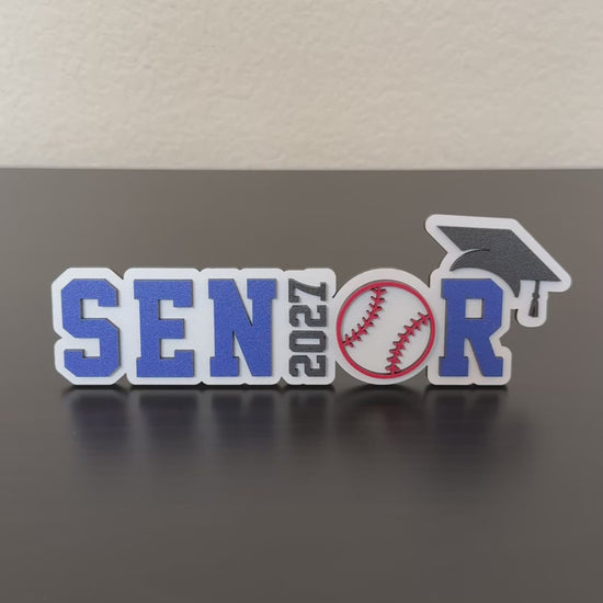 Video of Class of 2027 wood baseball graduation sign with blue and white lettering and baseball detail