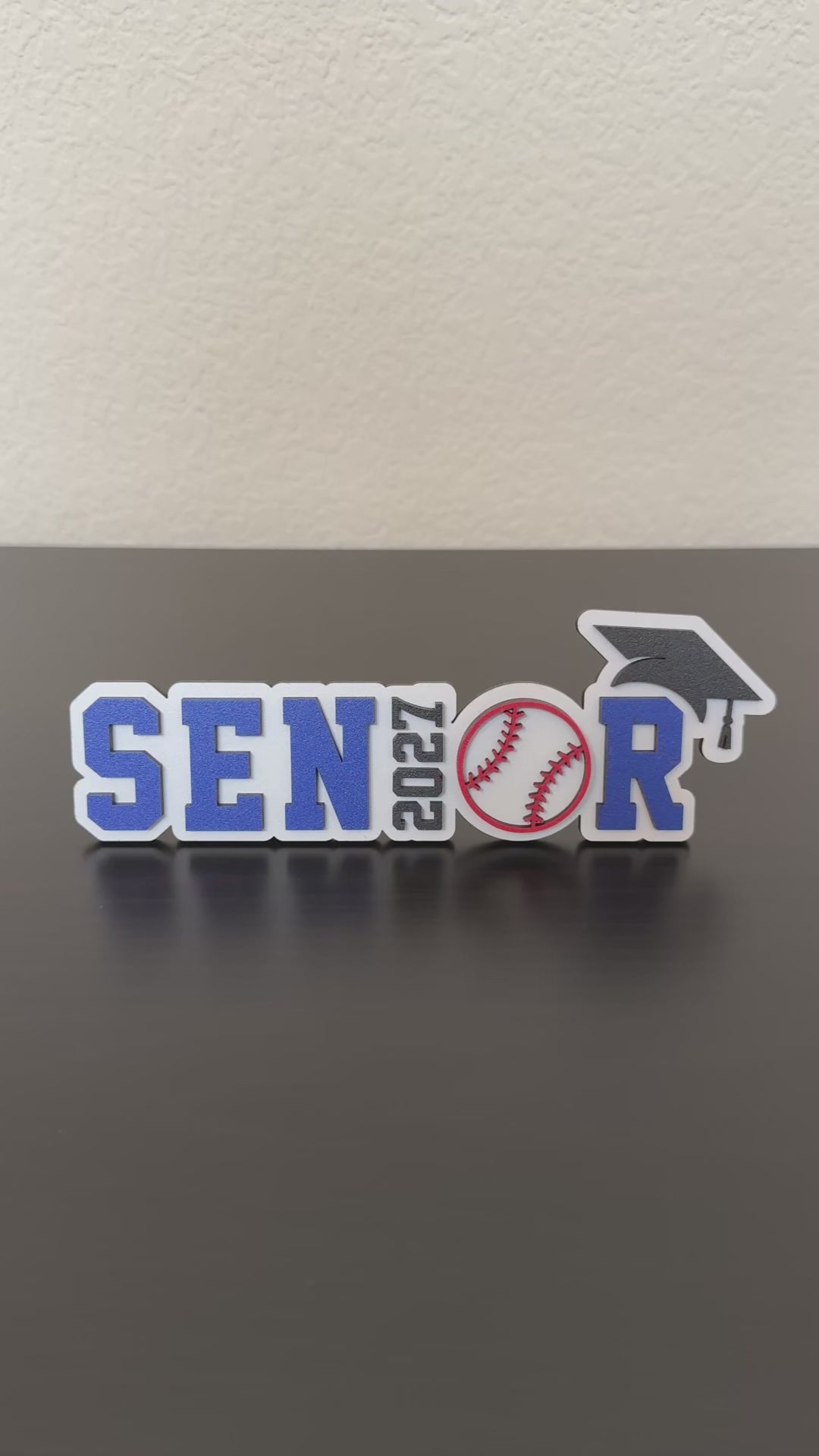 Video of Class of 2027 wood baseball graduation sign with blue and white lettering and baseball detail