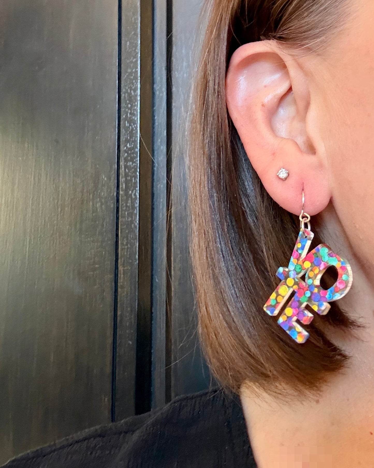 Model wearing VOTE earrings made from rainbow colored acrylic. These earrings spell vote.