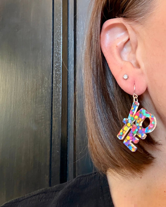 Model wearing VOTE earrings made from rainbow colored acrylic. These earrings spell vote.