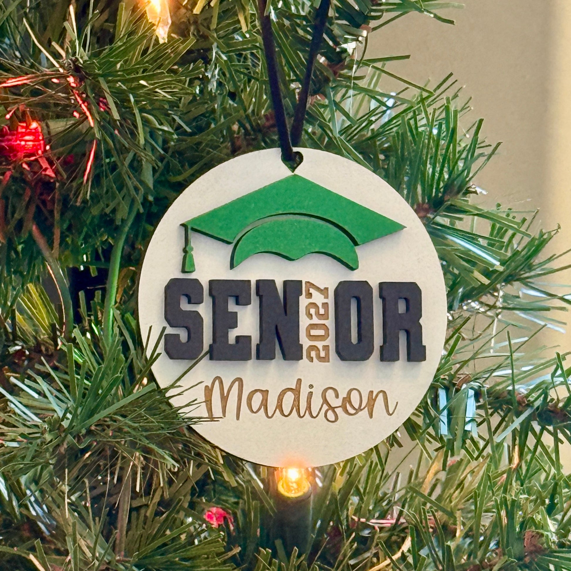 Personalized Senior 2027 wooden ornament in white with green graduation cap, engraved with the graduate's name