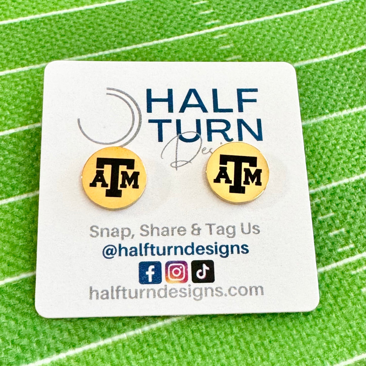 Texas A&M stud earrings engraved with the TAMU logo. The handmade earrings by Half Turn Designs are circular, 12mm in size and made from hypoallergenic Stainless Steel. Shown here in gold finish.