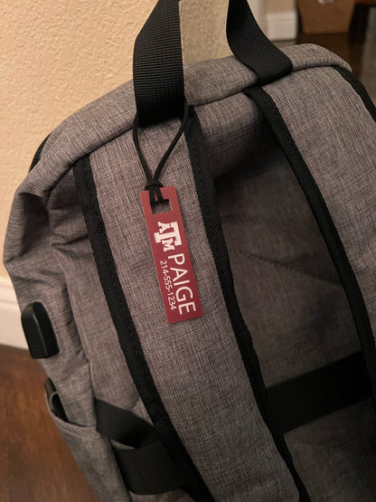 Officially licensed Texas A&M luggage and bag tags in rectangular shape, measuring 2.75x0.75".  These acrylic luggage and bag tags are personalized with 1-2 lines of text and come in 1/8" or 1/4" width.  Luggage tag colors include Clear, Frosted, Opaque Black, Shiny Black, Maroon that engraves white and Black that engraves white.  Maroon that engraves white shown here fastened to a backpack