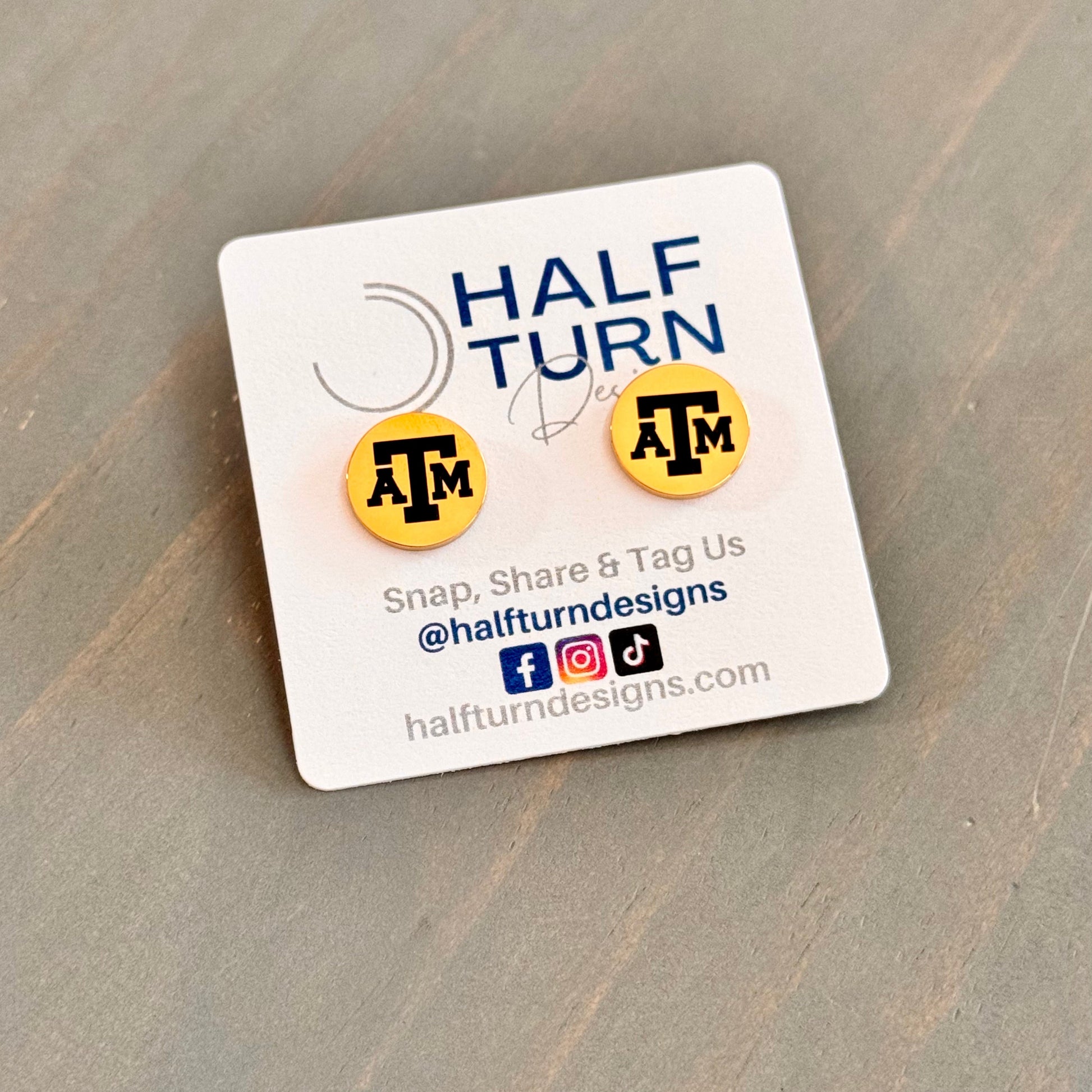 Texas A&M stud earrings engraved with the TAMU logo. The handmade earrings by Half Turn Designs are circular, 12mm in size and made from hypoallergenic Stainless Steel. Shown here in gold finish.