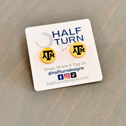Texas A&M stud earrings engraved with the TAMU logo. The handmade earrings by Half Turn Designs are circular, 12mm in size and made from hypoallergenic Stainless Steel. Shown here in gold finish.