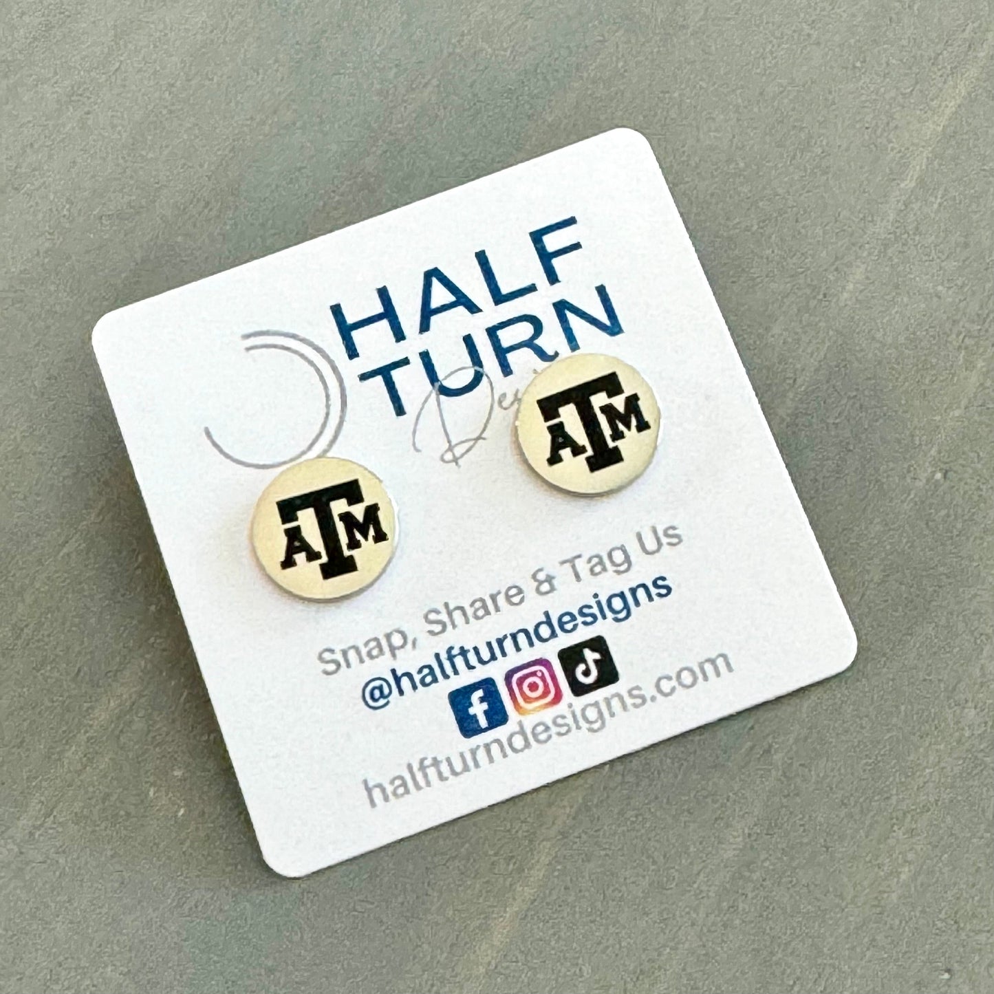 Texas A&M stud earrings engraved with the TAMU logo. The handmade earrings by Half Turn Designs are circular, 12mm in size and made from hypoallergenic Stainless Steel. Shown here in silver finish.
