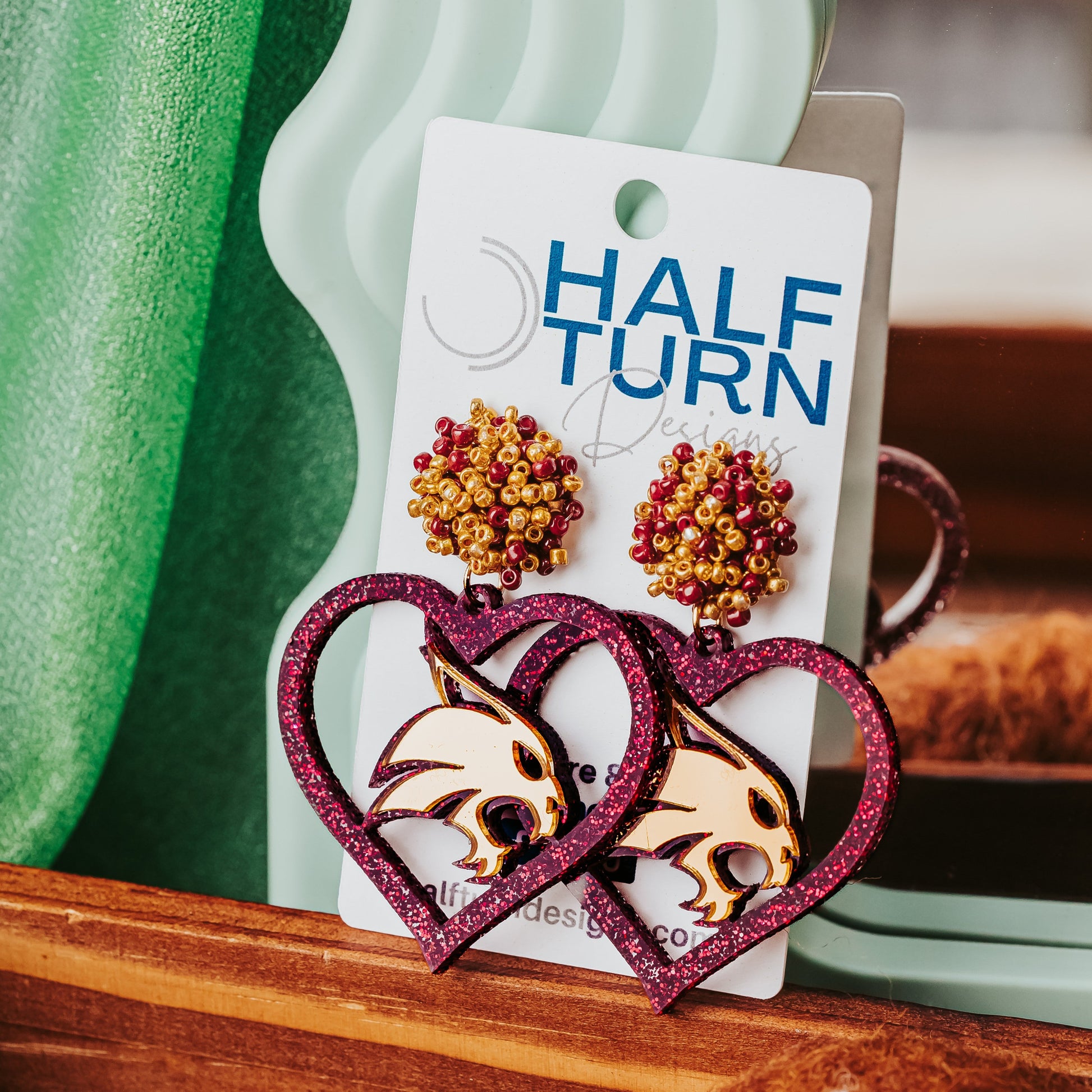 Texas State University Game Day Earrings. These earrings are maroon glitter acrylic hearts with gold mirror acrylic bobcats with maroon and gold beaded studs