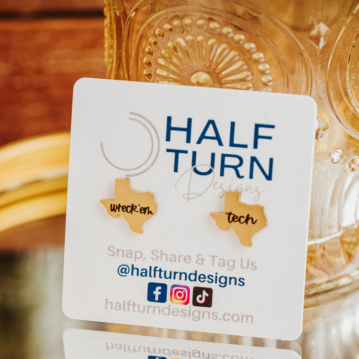 Gold-tone Texas Tech studs displayed on a branded card against a yellow vase on a mirror