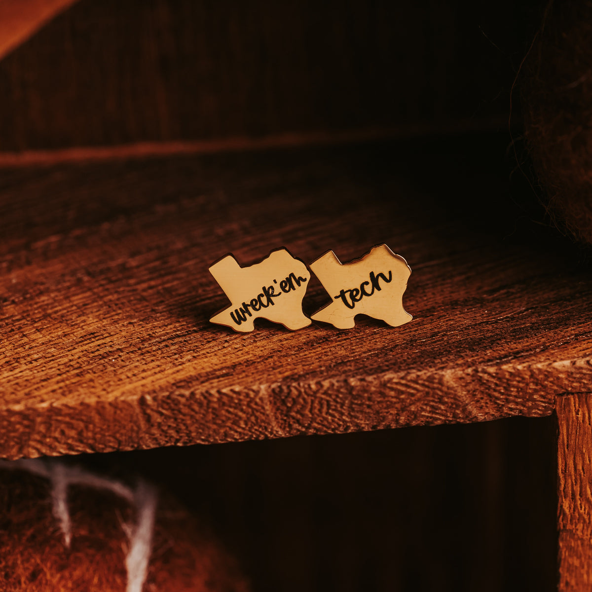 Gold-tone wreck'em and tech stud earrings in a dark wood cubby above a felted football