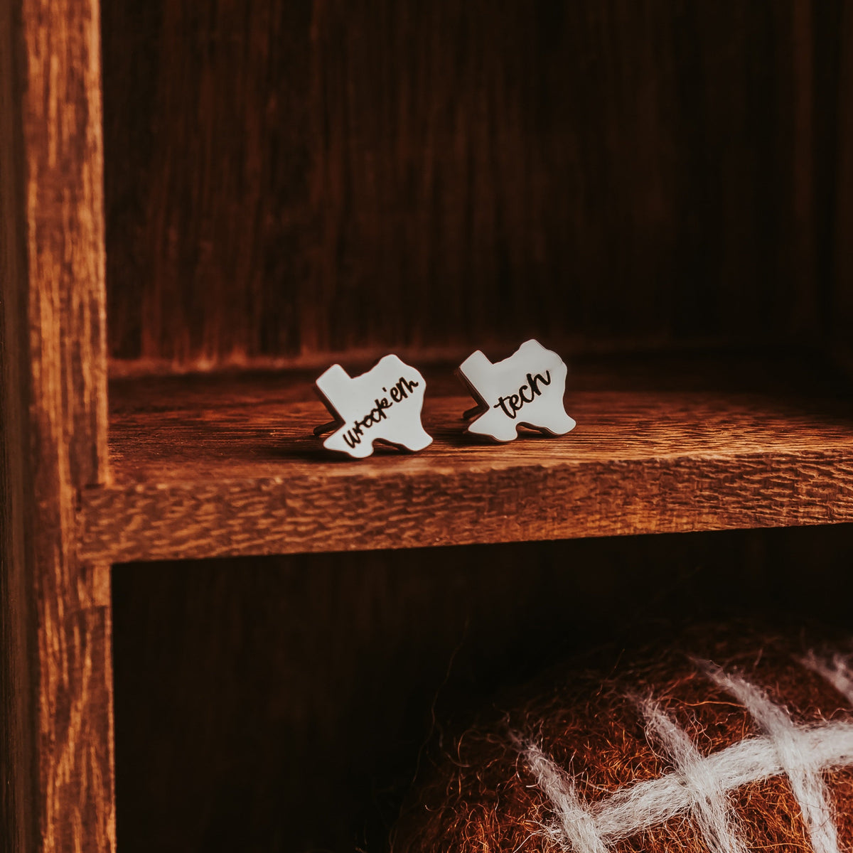 Silver-tone wreck'em and tech stud earrings in a dark wood cubby above a felted football