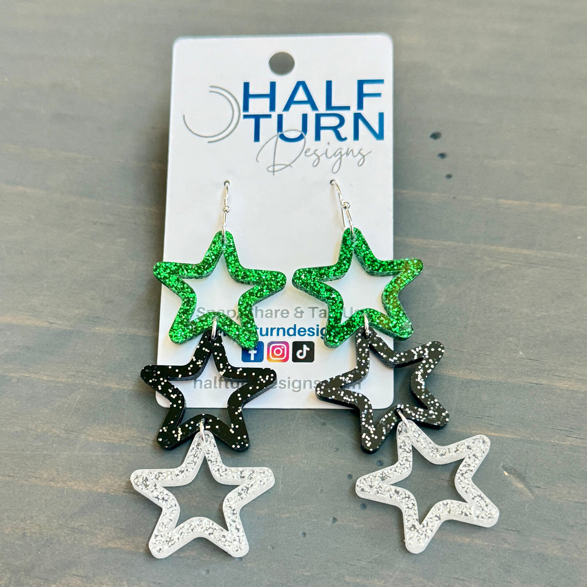Triple star dangle earrings—green glitter, black with white speckles, and silver-glitter acrylic—on silver hooks.