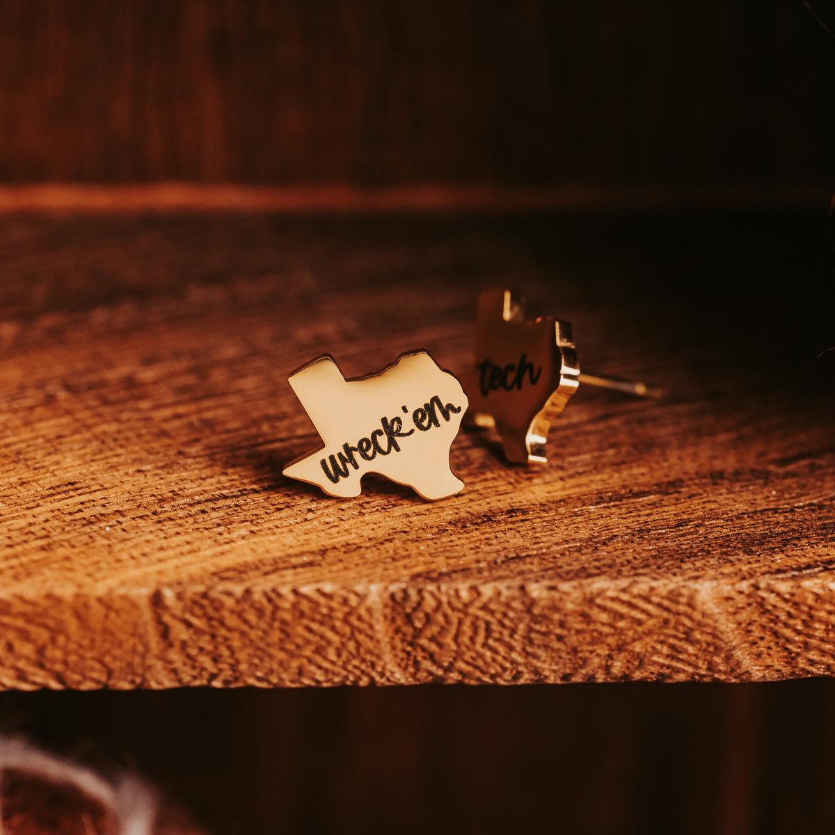 Close-up of Gold-tone wreck'em and tech stud earrings in a dark wood cubby above a felted football