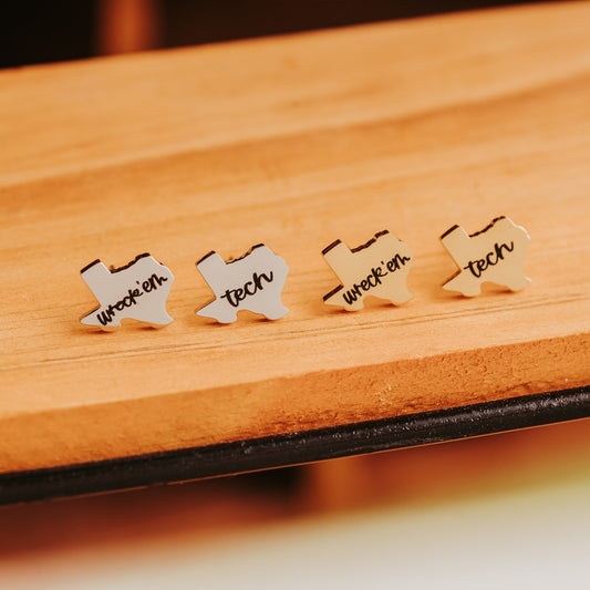Four Wreck 'Em Tech studs in a row on a pale wood shelf, showing the silver-tone and gold-tone finishes