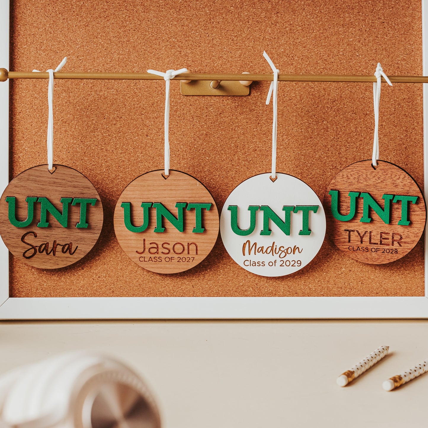 University of North Texas ornaments featuring green UNT letters with engraved personalization.  Shown in four wood types, from left to right, walnut, cherry, white and mahogany.  Officially licensed Mean Green personalized ornament by Half Turn Designs.