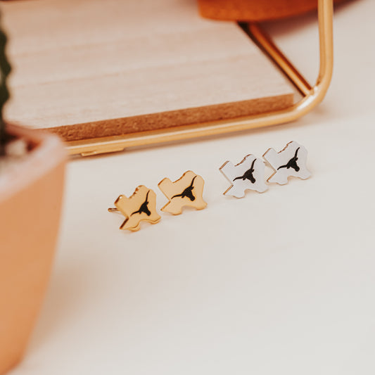 University of Texas stainless steel stud earrings shaped like the state of Texas, engraved with the Longhorn logo. Shown in 12mm size on Half Turn Designs branded earring cards, available in gold and silver finishes.